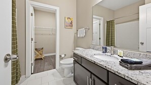 Une salle de bain avec des toilettes blanches, un lavabo doté d’un plan de travail en marbre et un grand miroir.
