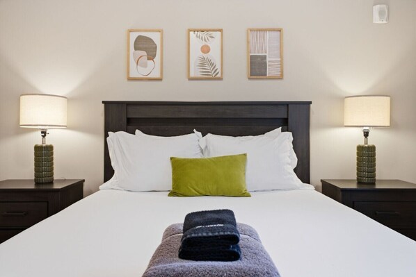 Habitación de hotel con una cama grande, dos mesitas de noche y tres cuadros enmarcados en la pared.