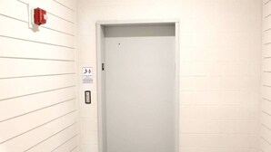 Puerta de ascensor blanca con detector de incendios y un cartel que indica prohibido fumar.