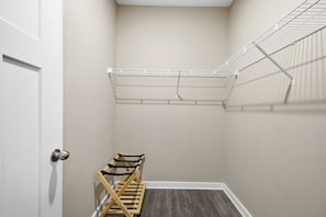 A small, enclosed room with a white door, a wooden bench, and a wire shelf.