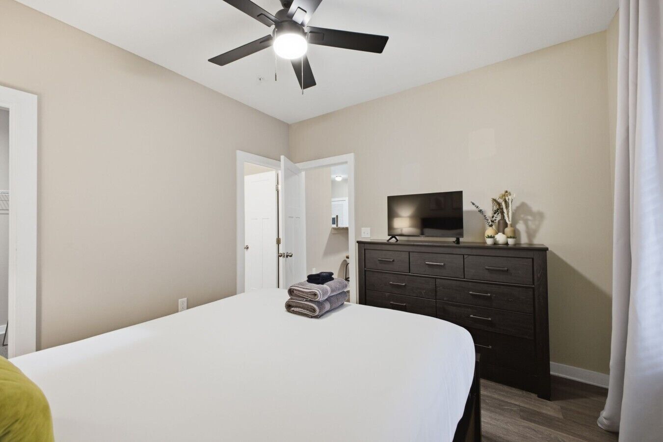 A bedroom with a bed, a dresser, a television, and a ceiling fan.