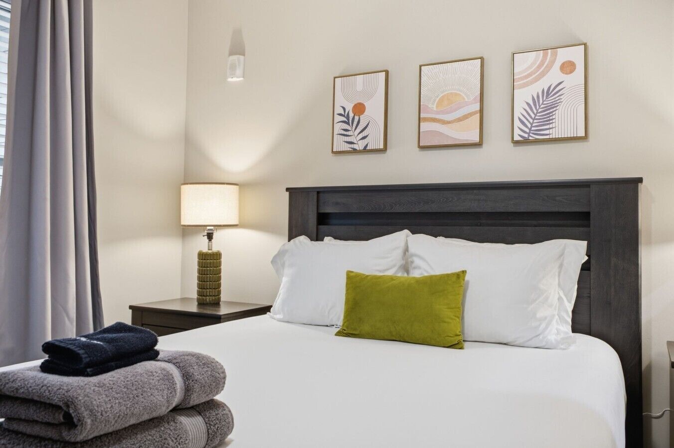 A hotel room with a bed, a nightstand, a lamp, and three wall art pieces.