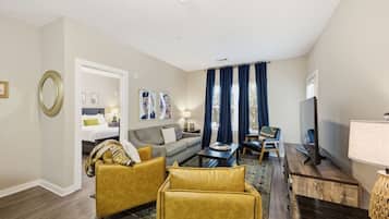 Een moderne hotelkamer met een bank, fauteuils, een salontafel, een televisie en een bed.