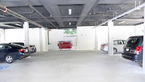 Un garaje para estacionar con pisos de concreto, paredes blancas y vigas metálicas. Hay automóviles estacionados a ambos lados.