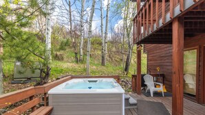 Un bain à remous sur une terrasse en bois, entouré d’une clôture en bois, d’arbres et d’un bâtiment doté d’une porte en verre.