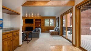 L’intérieur chaleureux d’un chalet, avec un revêtement mural en bois, une cheminée, un canapé et un téléviseur.