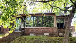 Une petite maison en briques avec de grandes fenêtres, un porche en bois et une cour gazonnée.