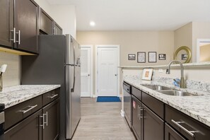 Eine moderne Küche mit dunklen Schränken, einem Edelstahl-Kühlschrank, Granit-Arbeitsplatten, einer Spüle und einer Rückwand.