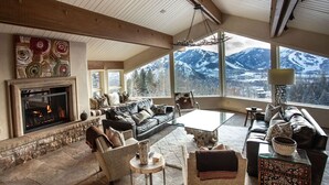 Ein gemütliches Wohnzimmer mit Kamin, bequemen Sitzmöglichkeiten und einem großen Fenster mit Blick auf die Berge.