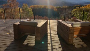 Eine Holzterrasse mit zwei gepolsterten Stühlen, die einen malerischen Blick auf Berge und einen See bietet.