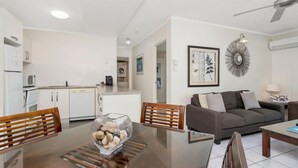 A modern living room with a sofa, coffee table, and a dining area with chairs and a glass-top table. - Seascape Holidays at The Queenslander Two Bed Standard (Port Douglas)