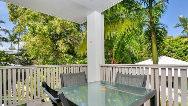 An outdoor patio with a glass table and chairs, surrounded by a white fence and lush greenery. - Seascape Holidays at The Queenslander Two Bed Standard (Port Douglas)