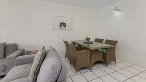 Un pequeño espacio de sala con un sofá, una mesa de comedor con sillas y una lámpara fijada a la pared.