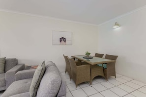 Un pequeño espacio de sala con un sofá, una mesa de comedor con sillas y una lámpara fijada a la pared.