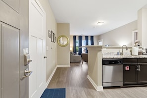 A modern kitchen with a dishwasher, a sink, and a countertop. There is a hallway leading to a living area with a sofa and a coffee table.
