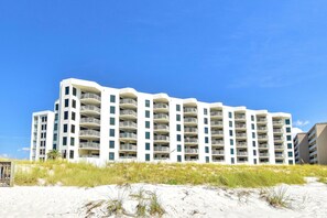 A multi-story hotel with balconies, located near a sandy beach.