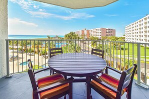 A balcony with a round table and chairs, overlooking a pool and a view of the ocean and buildings.