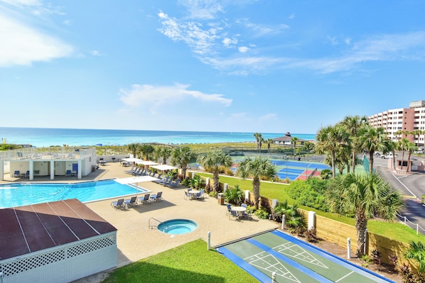 A resort with a swimming pool, tennis courts, and a view of the ocean.