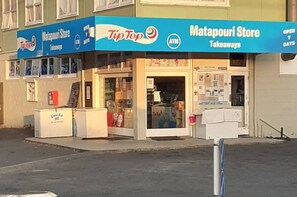 Un escaparate con un letrero azul que indica que es una tienda Matapouri que ofrece comida para llevar y un cajero automático.