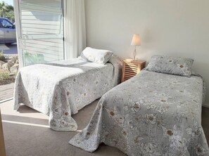 Un dormitorio con dos camas individuales, una mesita de noche con lámpara y una ventana con persianas.
