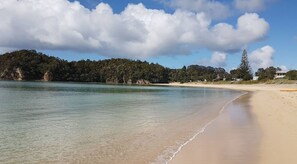 Una playa con agua cristalina, orilla arenosa y una colina boscosa al fondo.