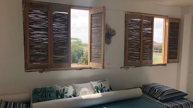 Una habitación con sofá cama, dos ventanas con persianas de madera y un adorno de mariposa en la pared.