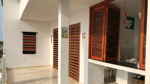 Un balcón amplio con suelo de baldosas, contraventanas de madera y una alfombra tejida de colores.