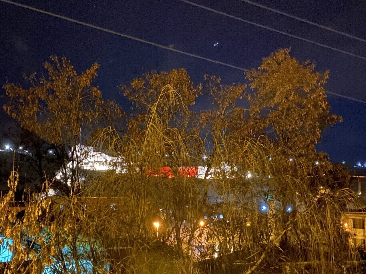 Vista nocturna de un edificio con ventanas iluminadas y un avión visible en el cielo.