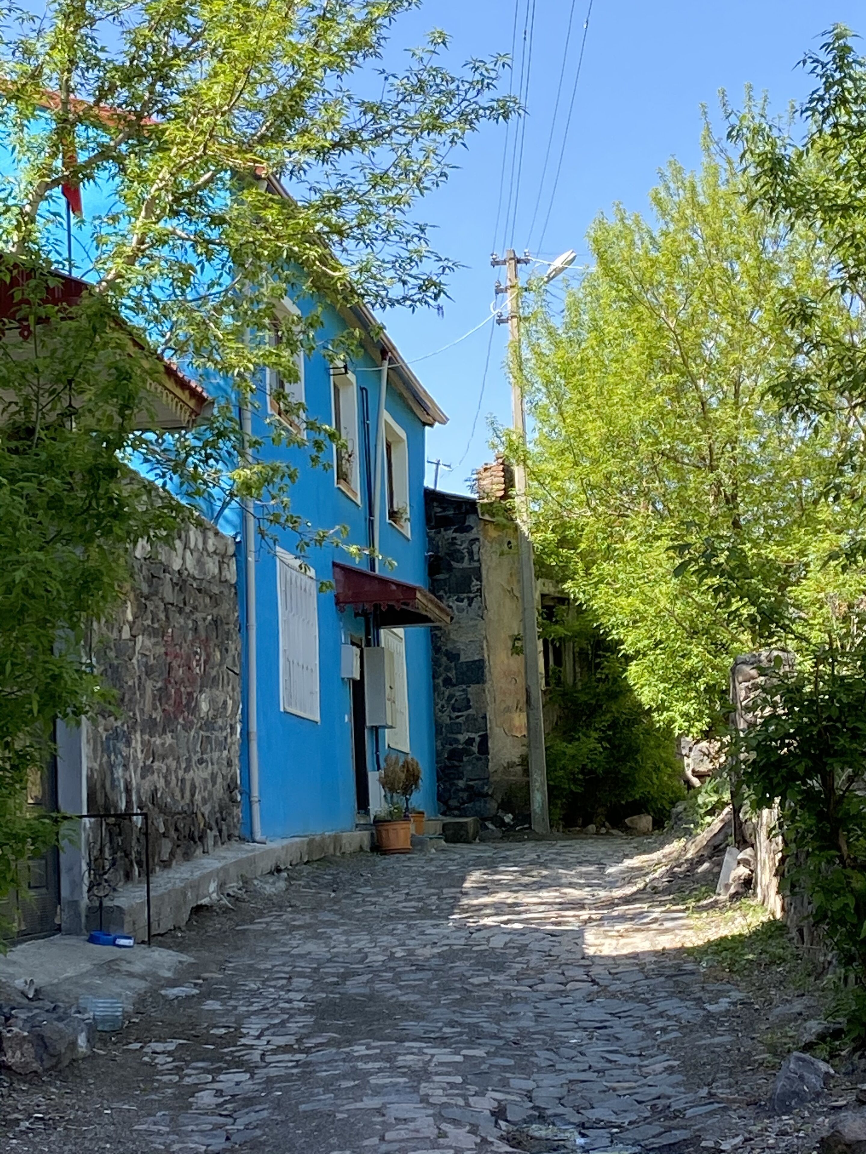 Uma rua de paralelepípedos estreita, ladeada por edifícios com paredes de pedra e fachadas azuis.