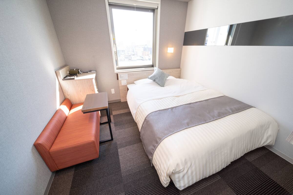 Ein modernes Hotelzimmer mit Bett, Bank, Schreibtisch und Fenster.