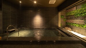 A spa area with a hot tub, tiled walls, and a rock garden with plants. - Super Hotel Premier Miyazaki Ichibangai (Miyazaki)