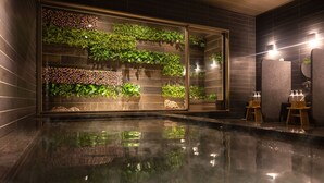 Un bany modern amb una paret de vidre que mostra vegetació exuberant, un paviment reflectant i un disseny minimalista.