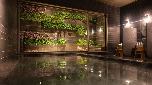 A modern bathroom with a glass wall displaying lush greenery, a reflective floor, and a minimalist design. - Super Hotel Premier Miyazaki Ichibangai (Miyazaki)