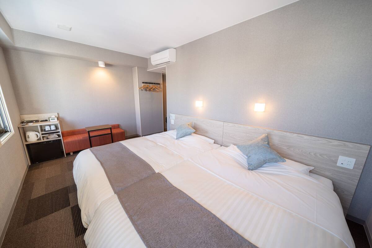 Ein Hotelzimmer mit einem großen Bett, einem Nachttisch, einem kleinen Schreibtisch mit Stuhl und einem Kleiderschrank.