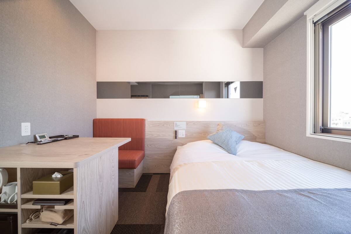 Ein modernes Hotelzimmer mit Bett, Schreibtisch, Stuhl und einer fest installierten Ablage.
