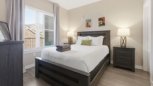 A bedroom with a bed, two bedside tables with lamps, a ceiling fan, and artwork on the wall.