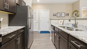 A modern kitchen with dark cabinets, a stainless steel refrigerator, granite countertops, and a built-in sink.