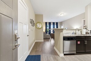 A modern kitchen with a dishwasher, a sink, and a countertop. There is a hallway leading to a living area with a sofa and a coffee table.