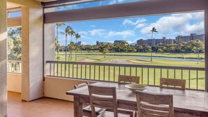 A balcony with a table and chairs, overlooking a golf course with buildings in the background.