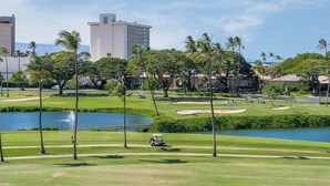 A golf course with a water body, palm trees, and buildings in the background.