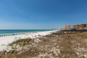 A beach with a wooden boardwalk leading to a building with multiple balconies. - Paradise Villa - Gulf Views, Private + Community Pools, Easy Beach Access! (Miramar Beach)