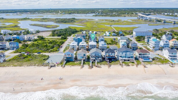 An aerial view of a coastal residential area with houses, a beach, and a bridge.