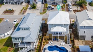 A residential area with multiple houses, a swimming pool, and a beach in the background.