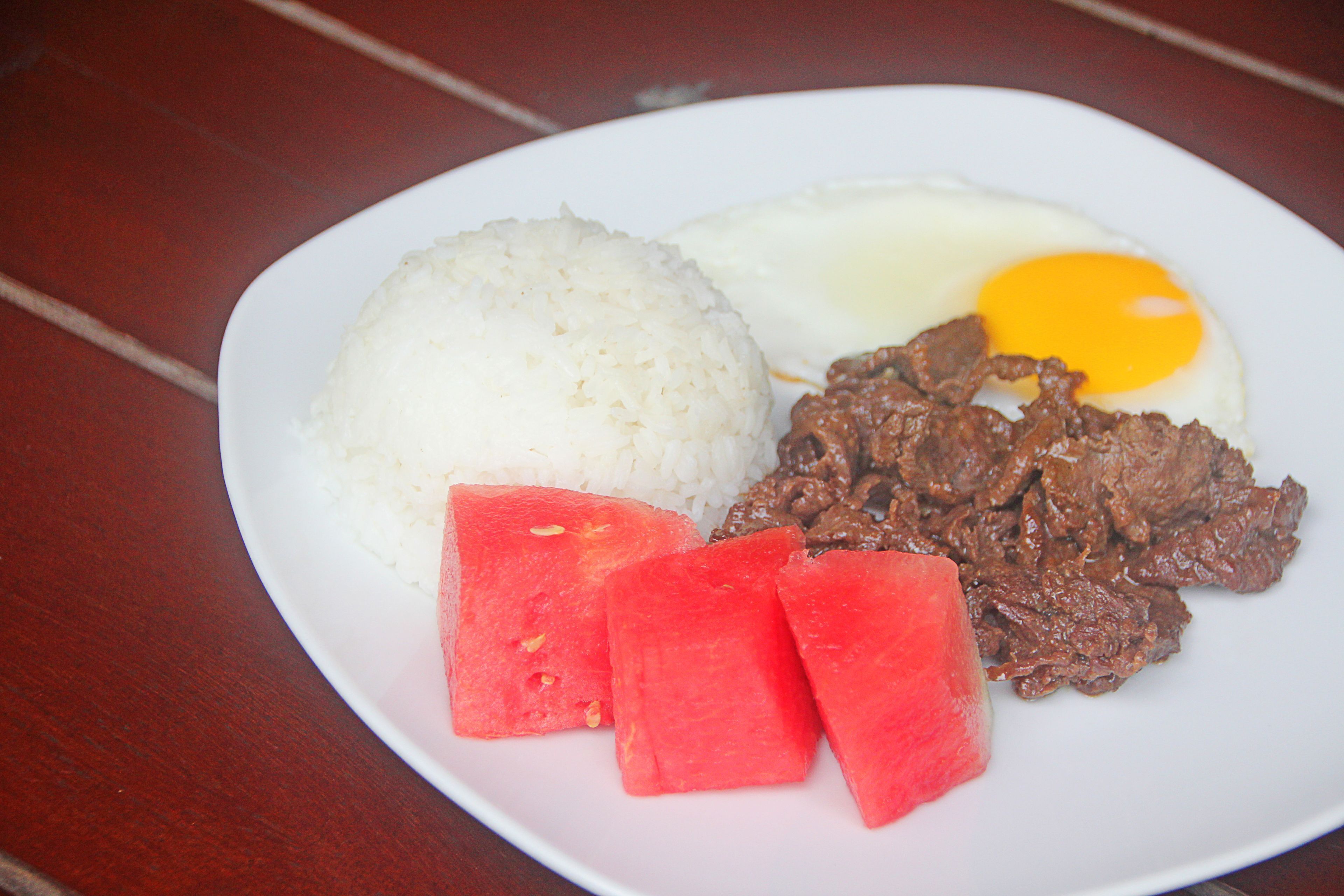 Un plato con arroz blanco, un huevo frito, carne de res y trozos de sandía.