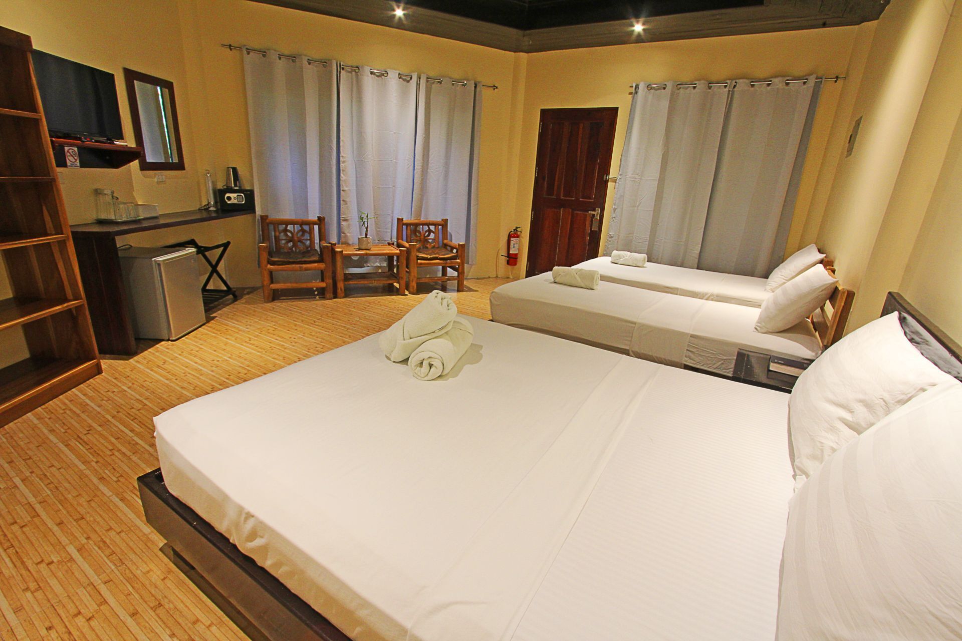 A hotel room with two beds, a desk, a chair, and a small kitchenette.