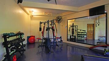 Uma academia com diversos equipamentos de exercícios, um espelho grande e uma porta com moldura de madeira.