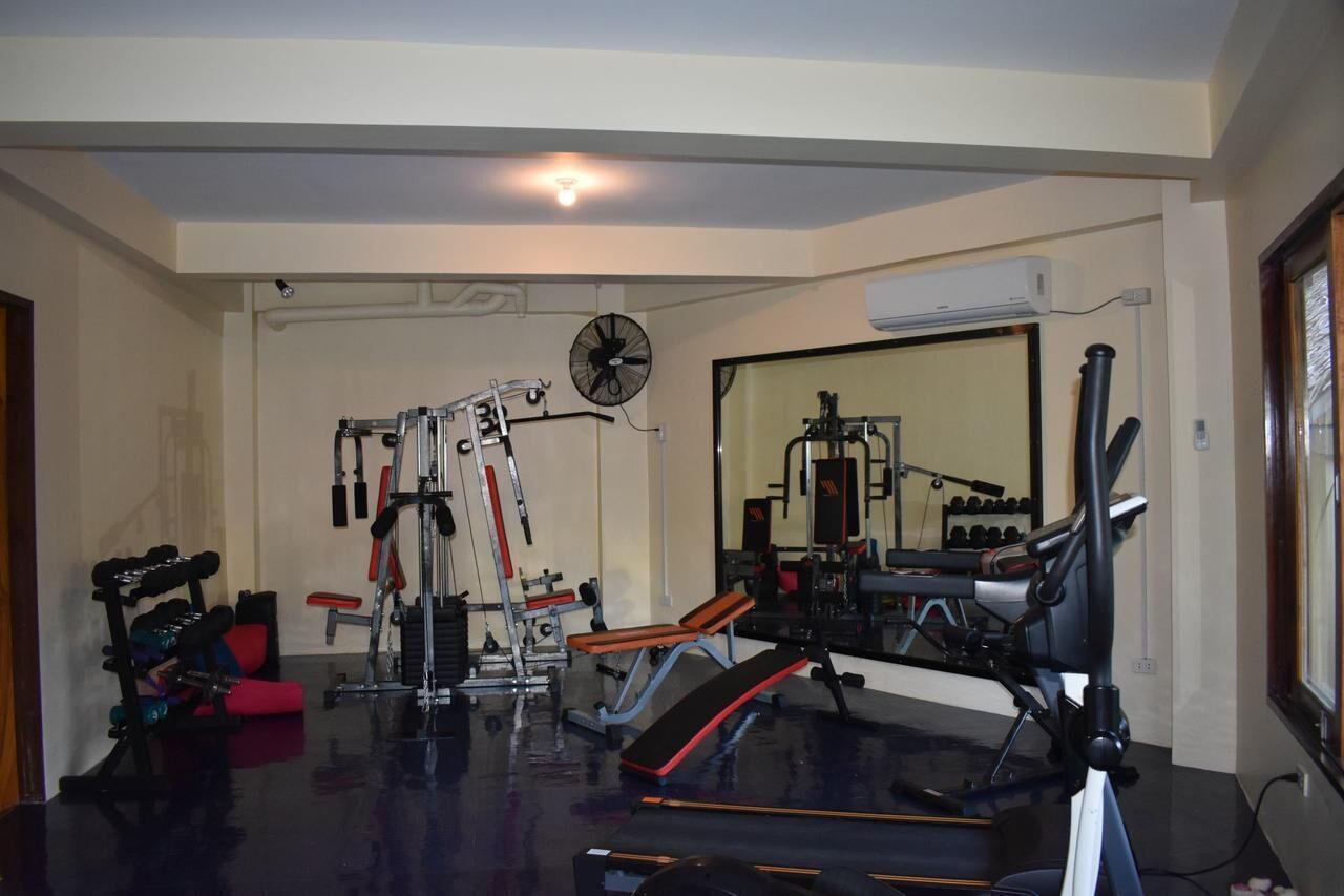 A home gym with various exercise equipment, including a bench, weight bench, and a fan.