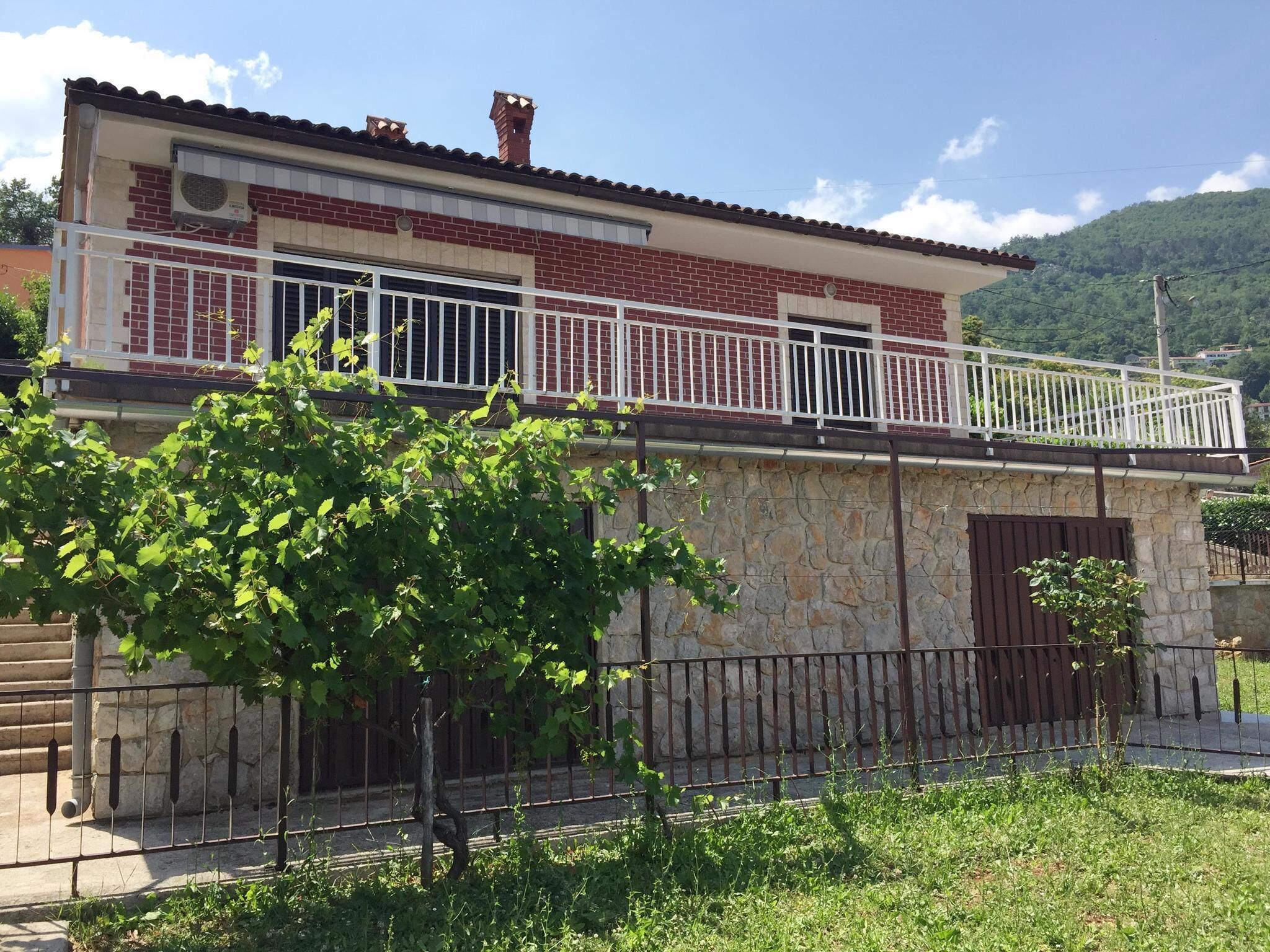 A two-story house with a balcony, stone walls, and a metal gate.