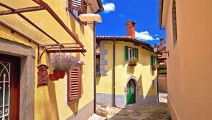 A narrow street with yellow buildings, a green door, and hanging flower baskets. - Holiday home with panoramic view and large terrace (Lovran)