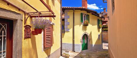 A narrow street with yellow buildings, a green door, and hanging flower baskets.